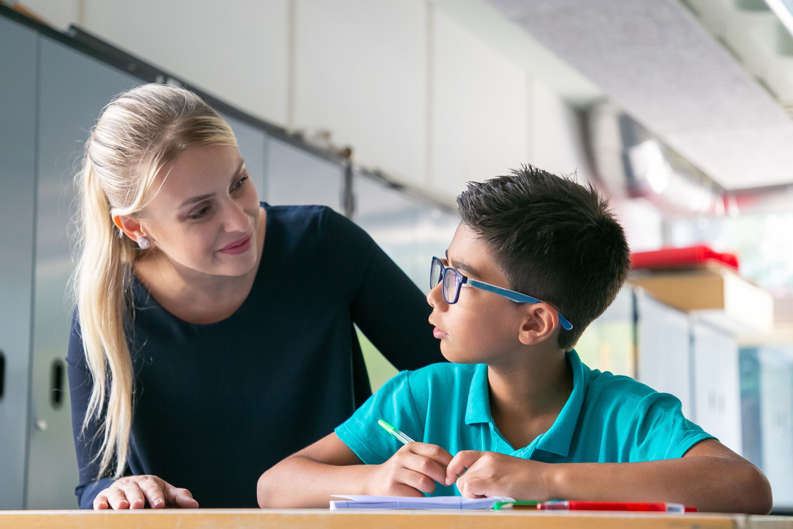 Cheerful school teacher giving help and support to schoolboy